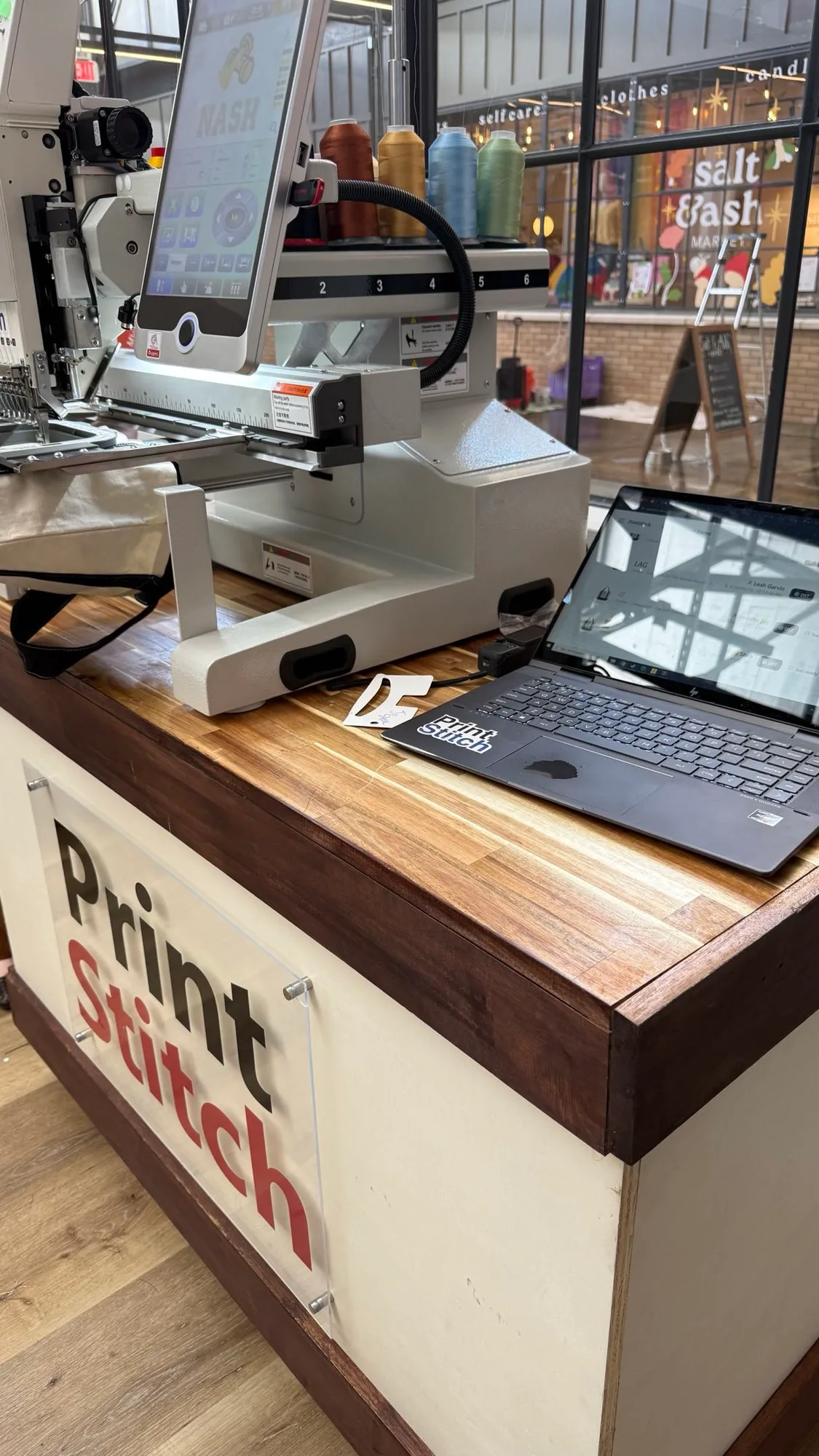 The PrintStitch live embroidery setup at the MVMT House event — machine, thread and the order list on a laptop