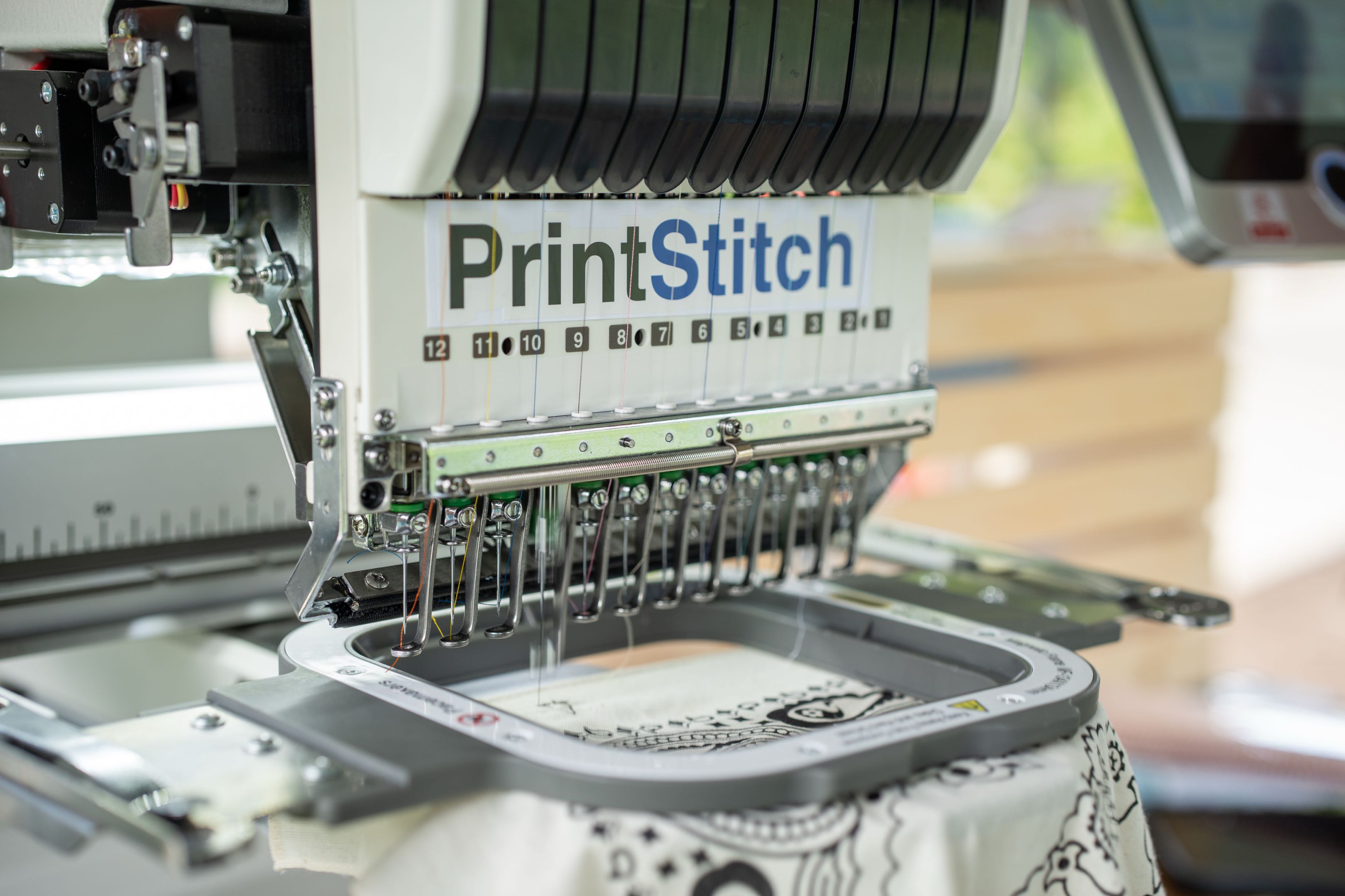 The PrintStitch twelve-needle embroidery machine stitching a custom bandana live at Solara Markets
